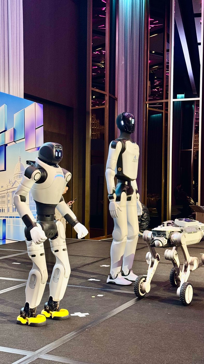 Two AGIBOT humanoid robots and a quadruped robot on a corporate event stage